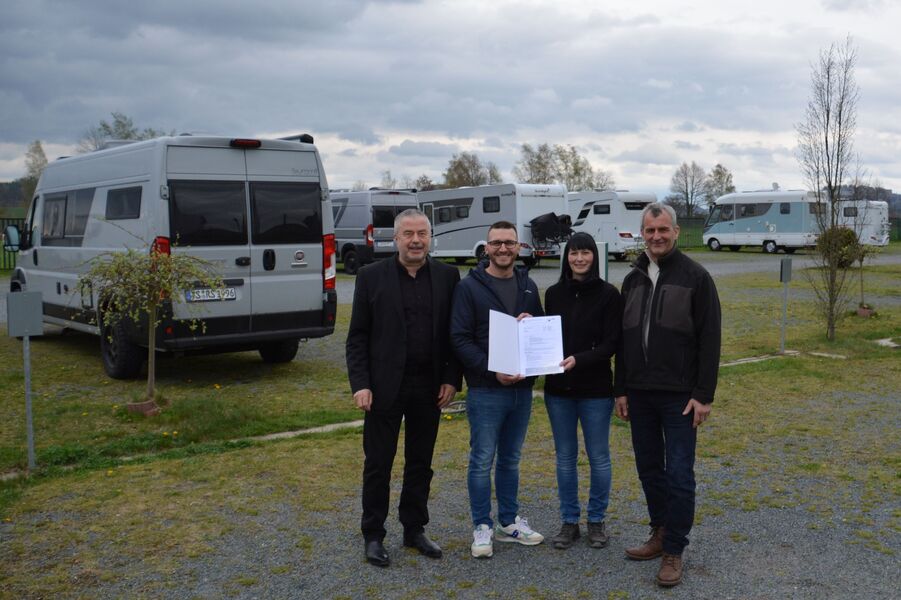 vier Personen auf einem Campingsplatz, im Hintergrund mehrere Campingwagen