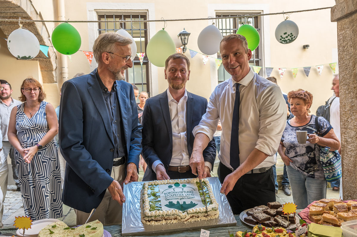 drei Männer in Anzügen schneiden eine Torte an
