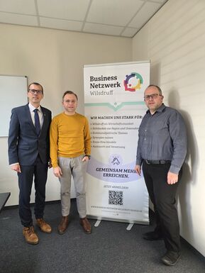 drei Männer stehen vor einem Roll Up