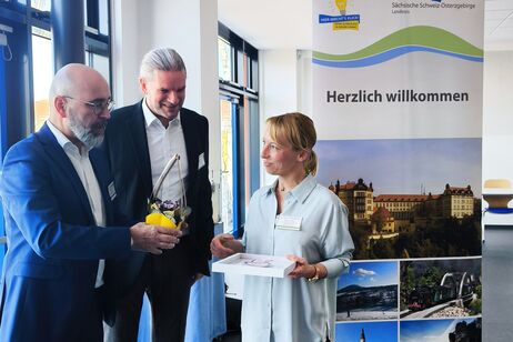 Die Vorsitzenden des Arbeitskreises SCHULEWIRTSCHAFT für den Bereich Wirtschaft, Axel Manthey, und für den Bereich Schule, Stefan Lustig, überreichen die Auszeichnung an Melanie Gäbel (Asklepios Klinik Neustadt in Sachsen).