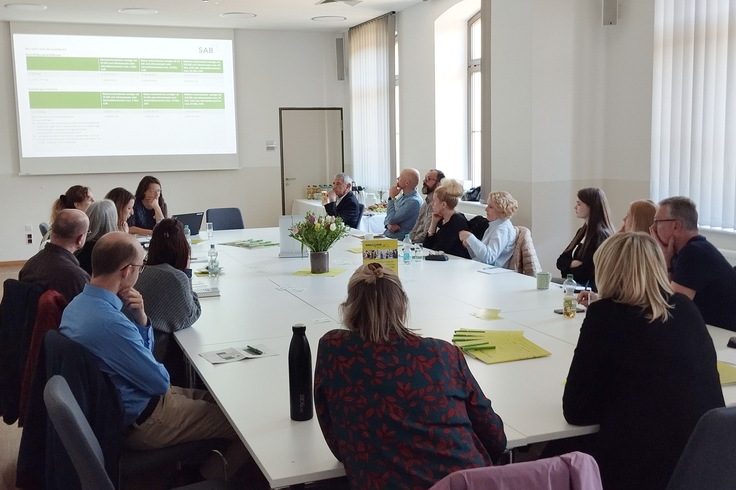Workshopteilnehmer am Tisch hören dem Vortragenden zu