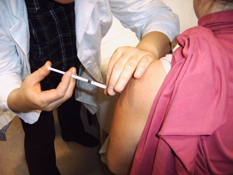 ein Mediziner setzt die Impf-Spritze an einer Patientin