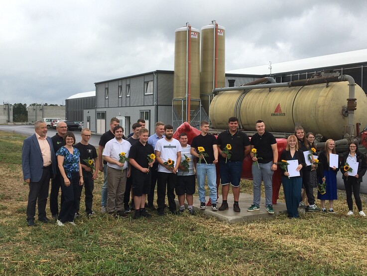 Lehrlinge mit Zeugnis und Blume in der Hand vor dem Stall